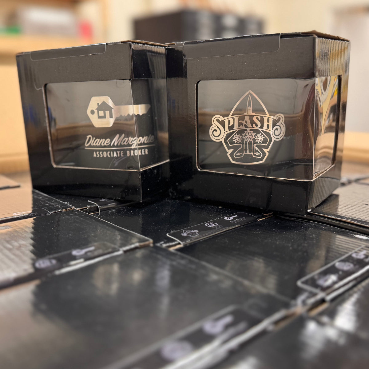 Two black engraved coffee mugs in black boxes. 