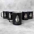 A black insulated mug with a clear lid and handle, featuring an engraved pine tree logo and the text 'Sequoia Springs' on the front, with five matching mugs arranged in the background on a light gray textured surface.