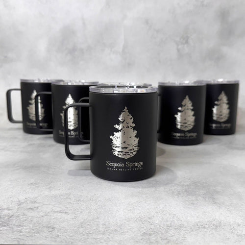 A black insulated mug with a clear lid and handle, featuring an engraved pine tree logo and the text 'Sequoia Springs' on the front, with five matching mugs arranged in the background on a light gray textured surface.