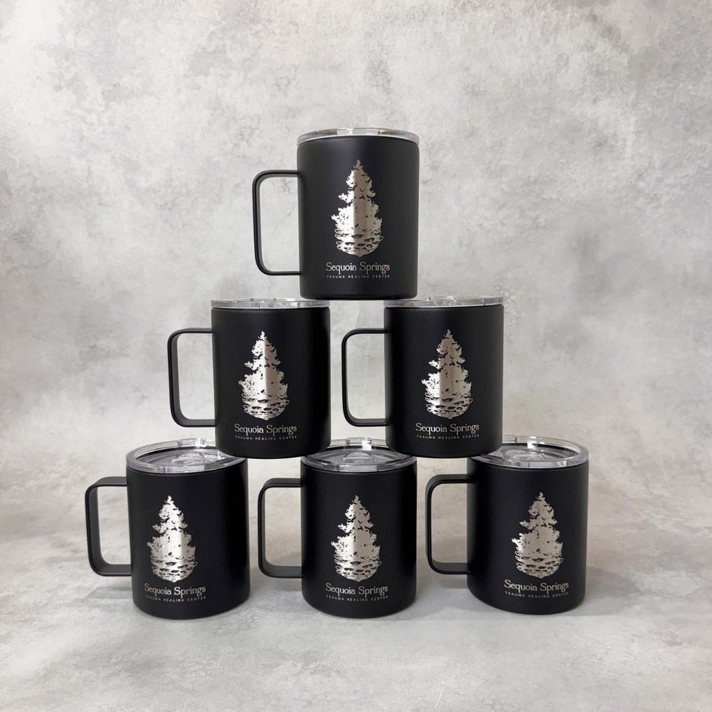 Six matte black insulated tumblers with clear lids are arranged in a pyramid on a light gray textured surface. Each tumbler has an engraved tree logo and the text 'Sequoia Springs.'