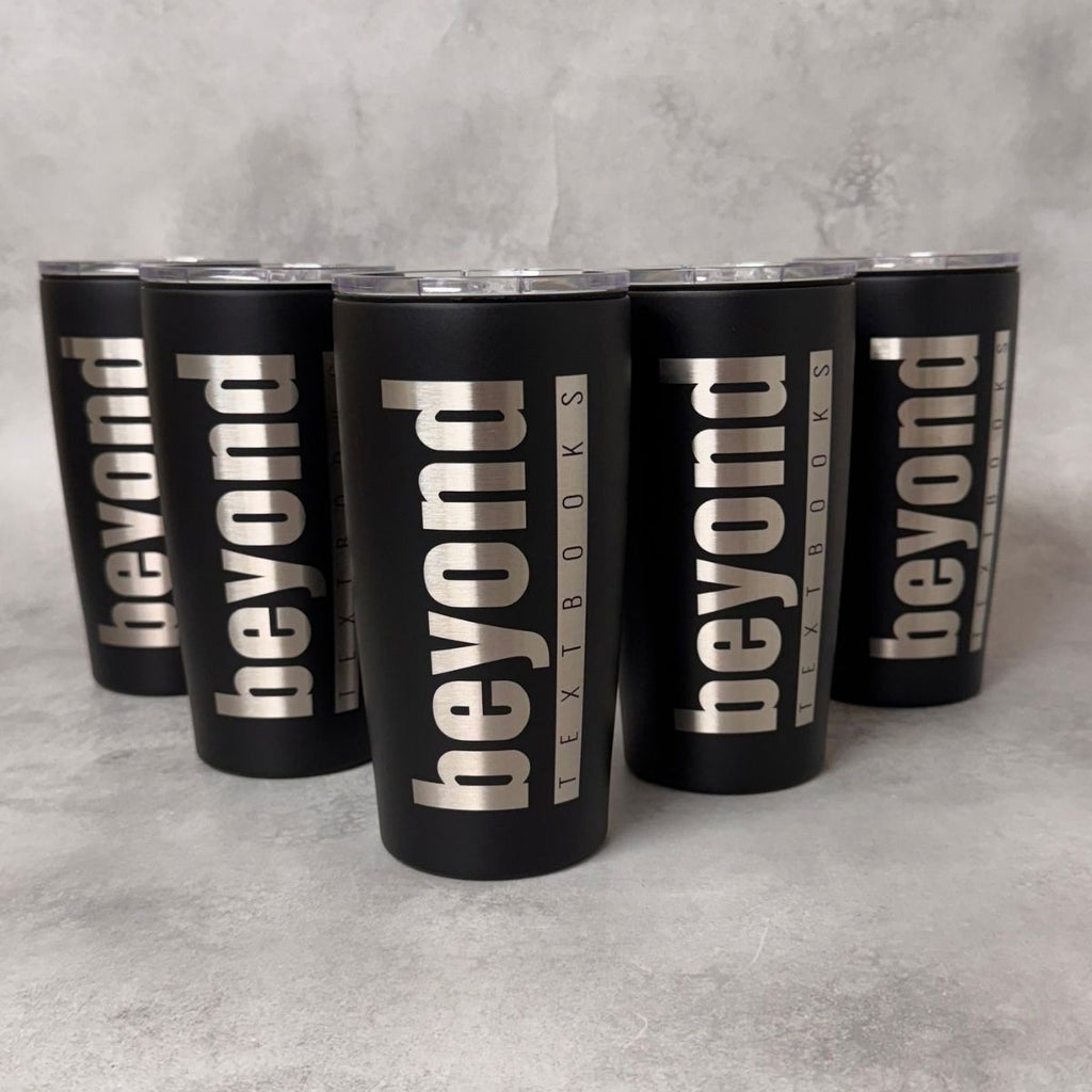 Five matte black insulated tumblers with clear lids arranged in a pyramid on a light gray textured surface. Each tumbler is printed vertically with the words "beyond" in large silver letters, with smaller text reading "TEXTBOOKS" running alongside.