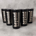 Five matte black insulated tumblers with clear lids arranged in a pyramid on a light gray textured surface. Each tumbler is printed vertically with the words "beyond" in large silver letters, with smaller text reading "TEXTBOOKS" running alongside.