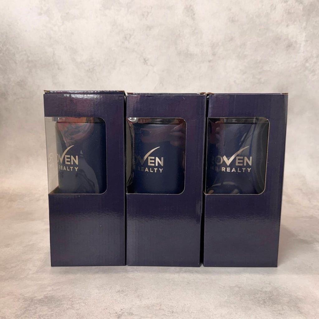 Three navy blue tumbler boxes with clear window cutouts, each displaying the 'Proven Home Realty' logo, arranged side-by-side in their matching dark navy retail packaging boxes against a textured gray background.
