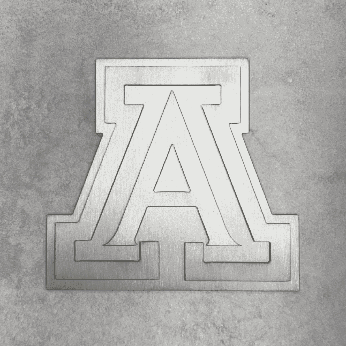 A brushed silver metal collegiate letter 'A' emblem, representing University of Arizona, mounted on a textured gray concrete wall.
