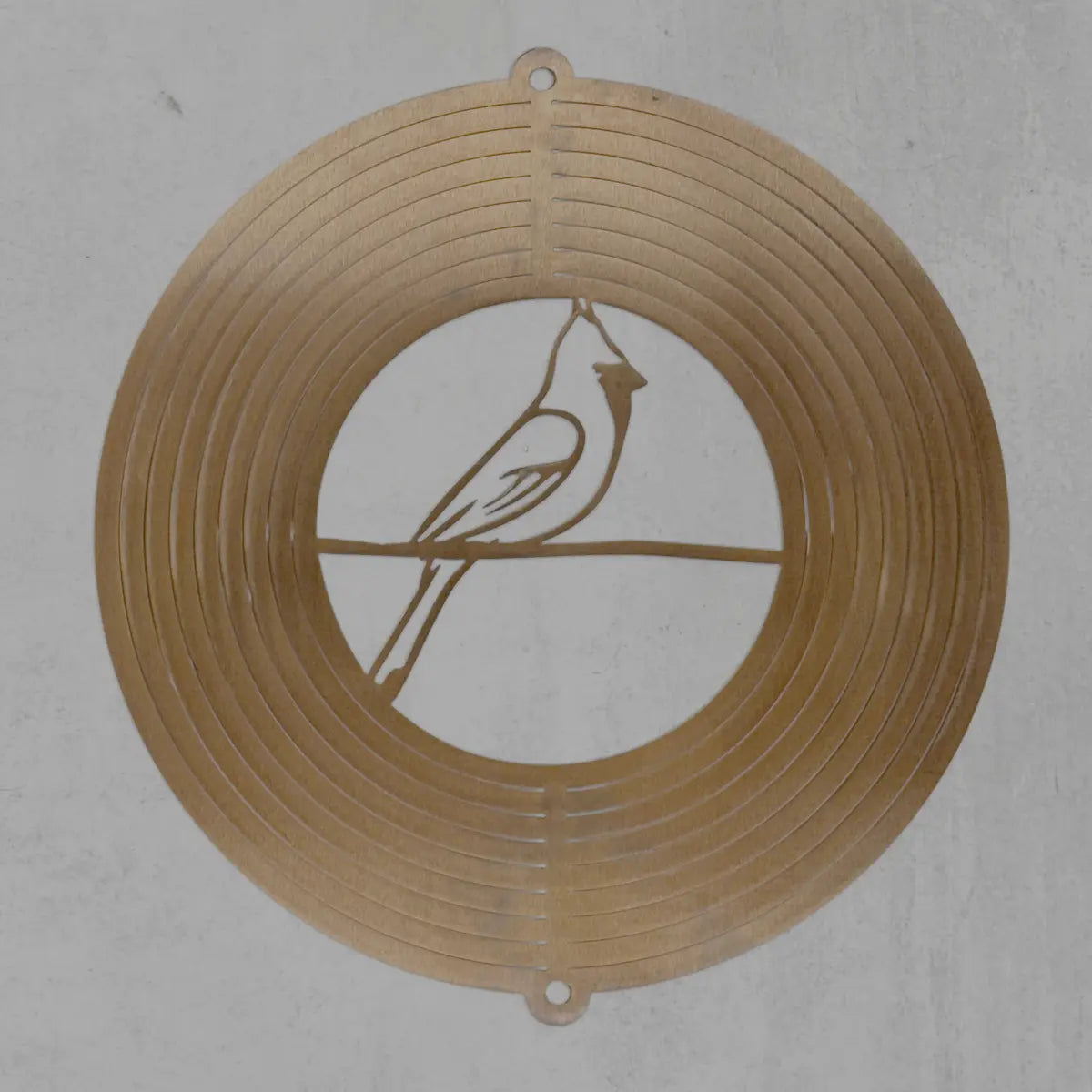 A circular metal wall art piece featuring a cardinal bird silhouette on a branch, displayed against a textured light gray background.