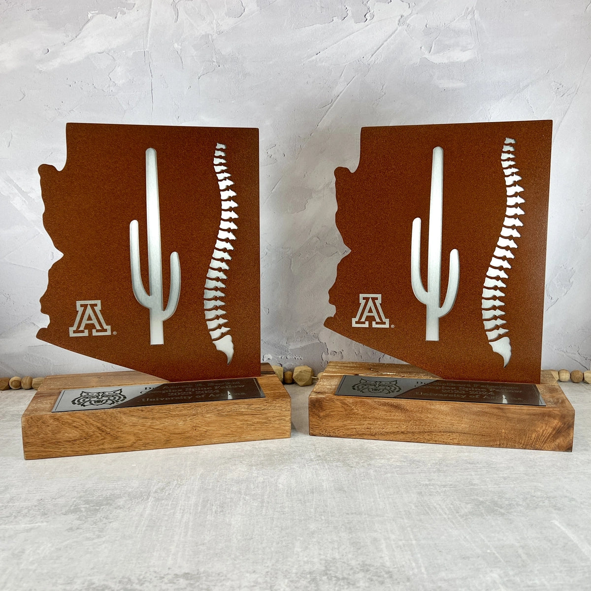 Two mesquite wood and rusted metal awards with the U of A logo and a spine cut out of the rusted metal, showing the gray steel beneath.