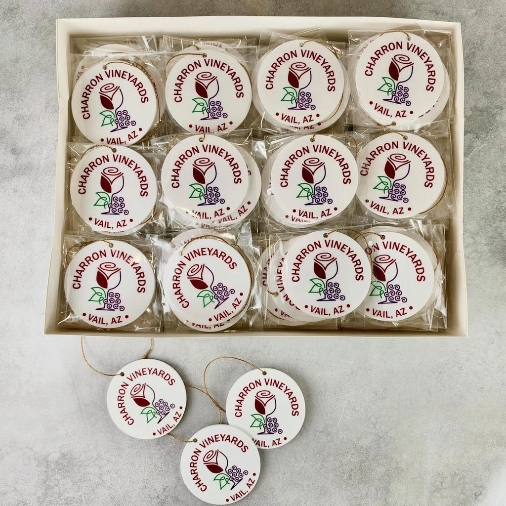 A boxed set of round white ornaments with printed 'Charron Vineyards' logos and grape illustrations, arranged in a tray with several additional ornaments placed in front on a light stone surface.