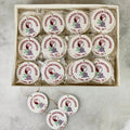 A boxed set of round white ornaments with printed 'Charron Vineyards' logos and grape illustrations, arranged in a tray with several additional ornaments placed in front on a light stone surface.