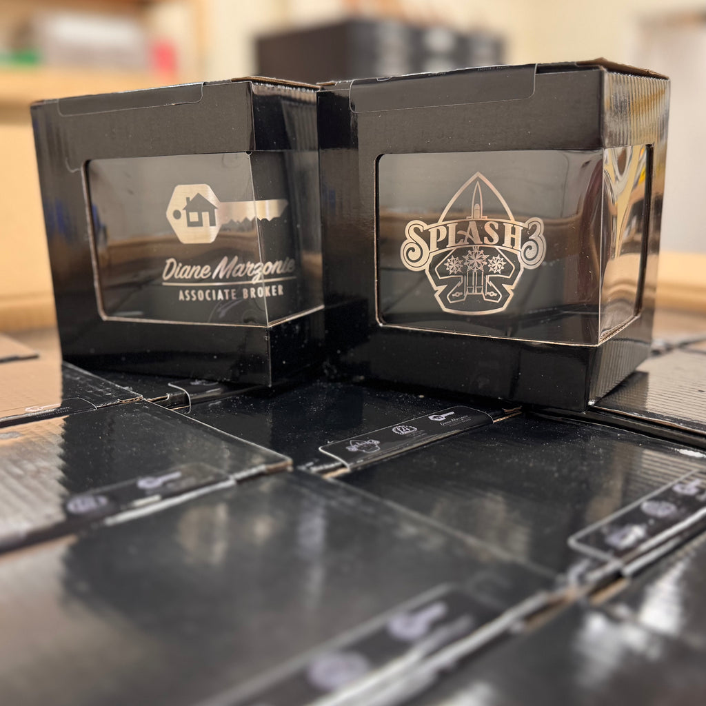 Two black engraved coffee mugs in black boxes. 
