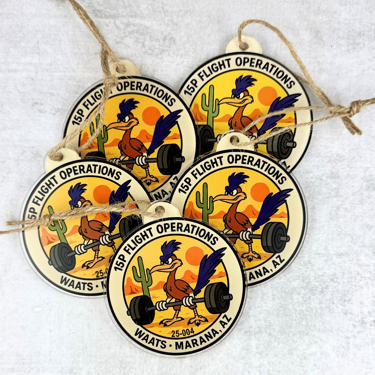 Five round hanging ornaments with twine loops, featuring a cartoon rooster lifting a barbell and the text '15th Flight Operations' and 'Waats - Marana, AZ' on a light textured background.