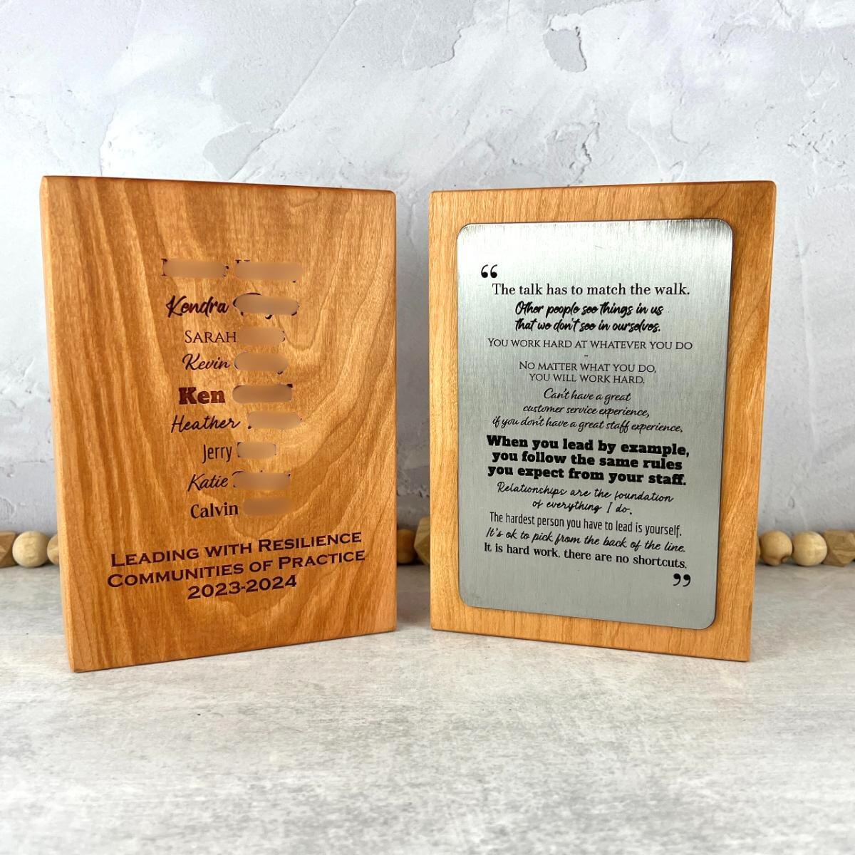 Two wooden plaques with engraved text on front and back. Front of plaque has a metal plate for decoration. 