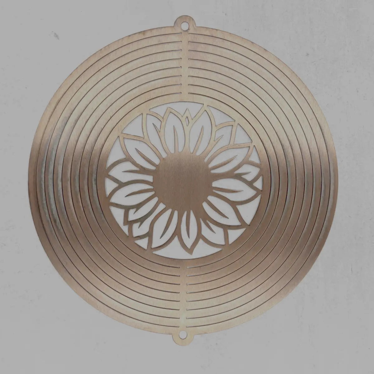 A circular metal wall art piece with concentric rings and a central sunflower cutout, shown against a neutral gray background.