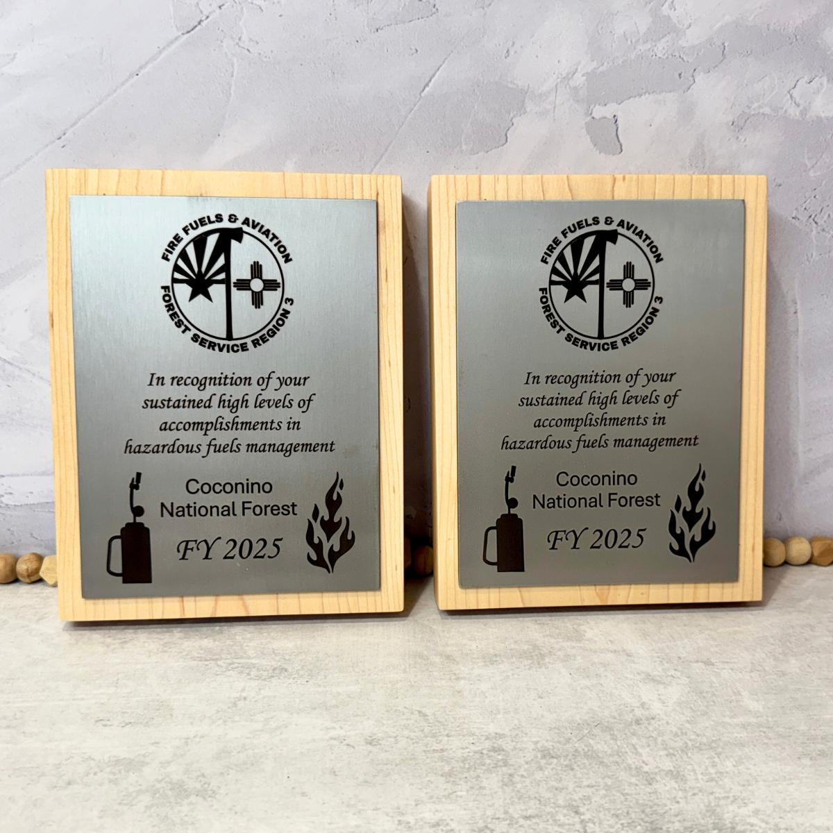Two wooden plaques with engraved text and a logo on a metal surface. 