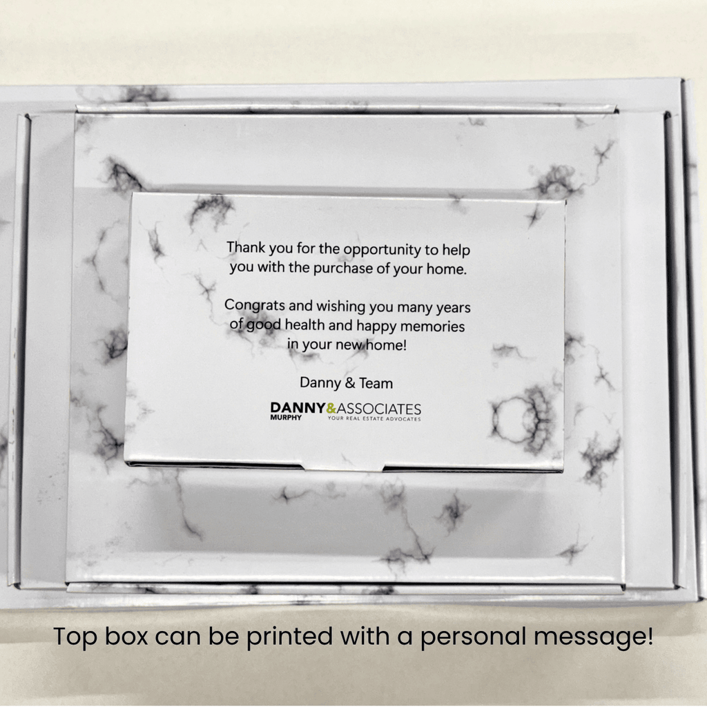 A white marble-patterned keepsake box with a printed message on the top. The card reads a congratulatory message for a home purchase and includes the brand name Danny & Associates.