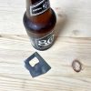 small raw metal bottle opener on wood counter next to a bottle