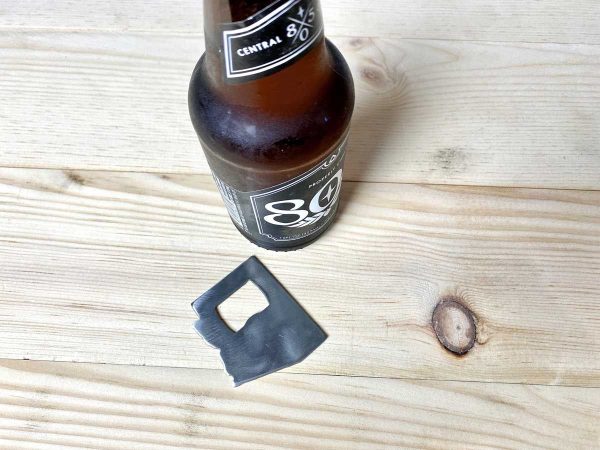 small raw metal bottle opener on wood counter next to a bottle