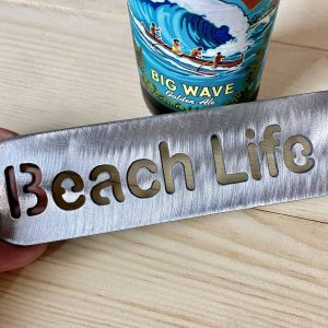 Beach life bottle opener in raw steel laying on a table.