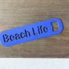 Beach life bottle opener in blue leaned against a bottle