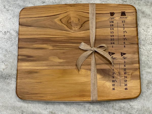 wood cutting board with measurement conversions engraved on the right side. Brown ribbon is tied around the right side of the board