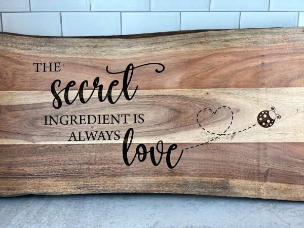 close up of a cutting board laser engaved with the message the secret ingredient is always love"