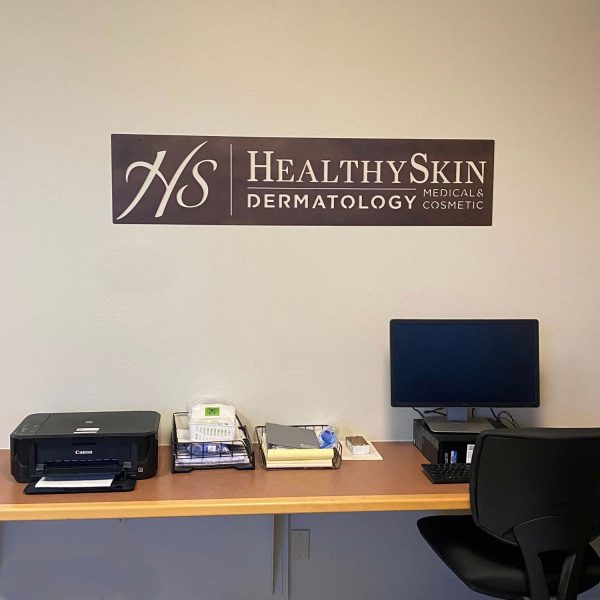 custom metal business sign for Healthy Skin Dermatology. Sign is mounted on a cream wall with a desk at the bottom of the image
