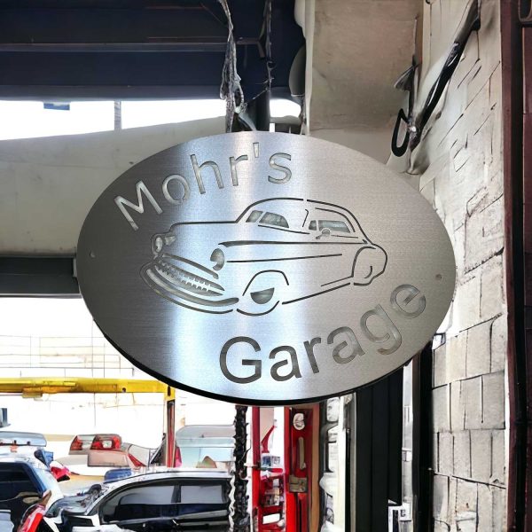 AI enhanced image of the brushed metal sign for Mohr's Garage. Appears to be hanging in front of a garage.