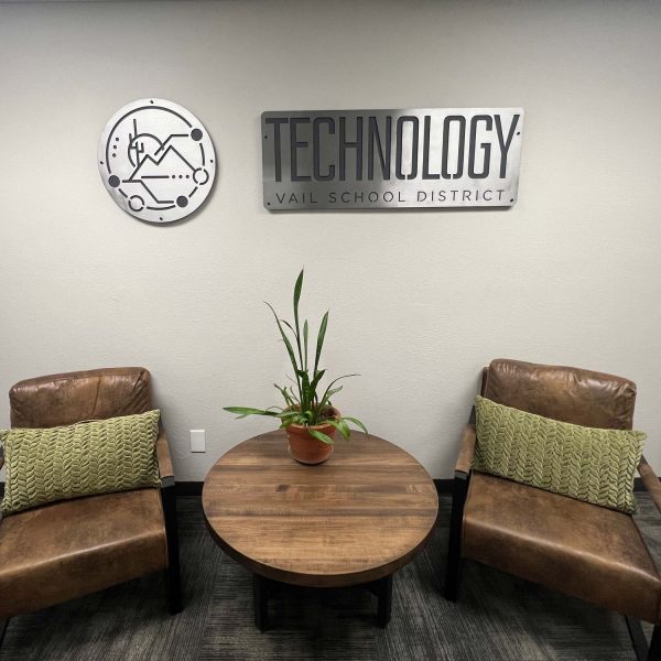 small lobby with brown chairs and green pillows. The signs on the wall are double layered metal, says "Technology" and the second sign is the logo.