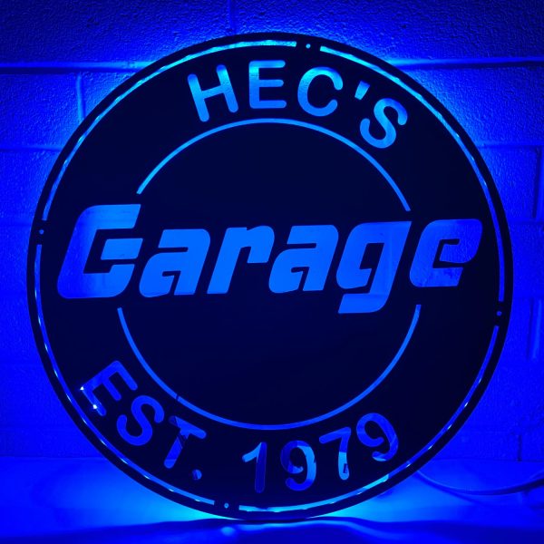lighted metal sign that says Hec's Garage, blue light coming from the back