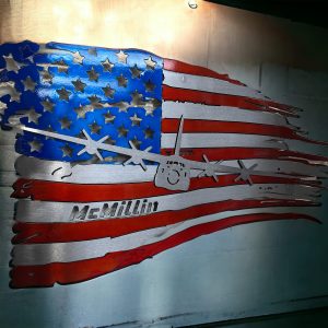 Red, silver, and blue tattered metal flag with airplane layered on top and name cut out.